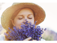 Mulher de chapéu de palha cheirando buquê de flores de lavanda com os olhos fechados.