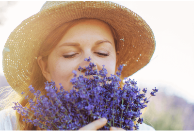 Mulher de chapéu de palha cheirando buquê de flores de lavanda com os olhos fechados.